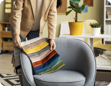 A person compares fabric swatches with a light blue armchair.